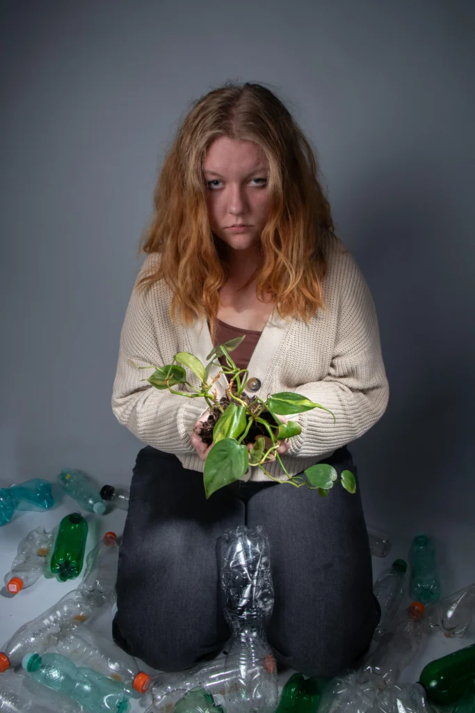 Fotografie dívky s depresivním výrazem držící rostlinu obklopenou plastovými odpadky